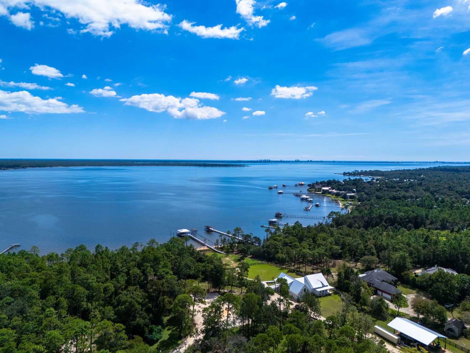 Stunning aerial view of a vast blue lake surrounded by lush green trees under a bright blue sky.