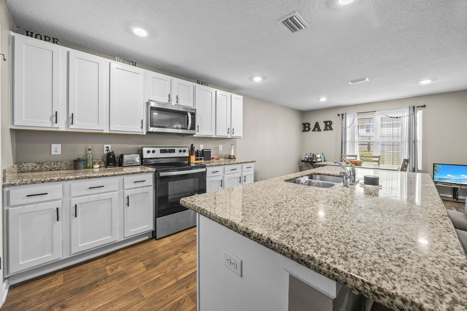 Modern kitchen with white cabinets, granite countertops, stainless steel appliances, and an open bar area with natural light.