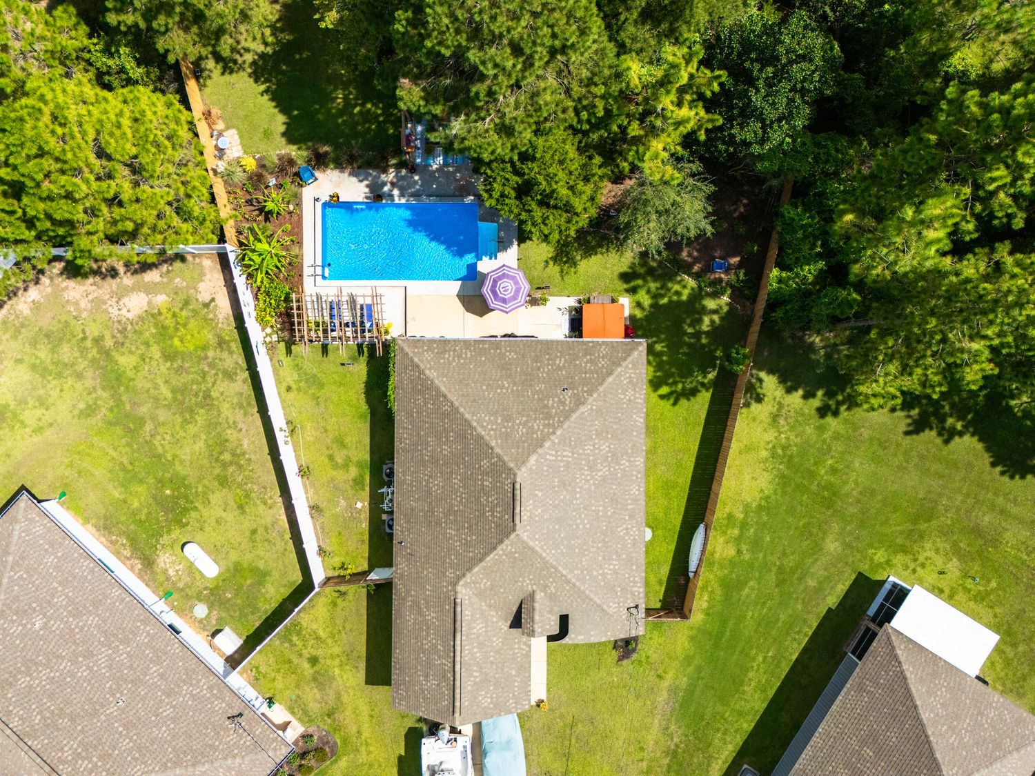 Aerial drone view of a suburban home with a gray roof, lush green lawn, and a rectangular backyard swimming pool.