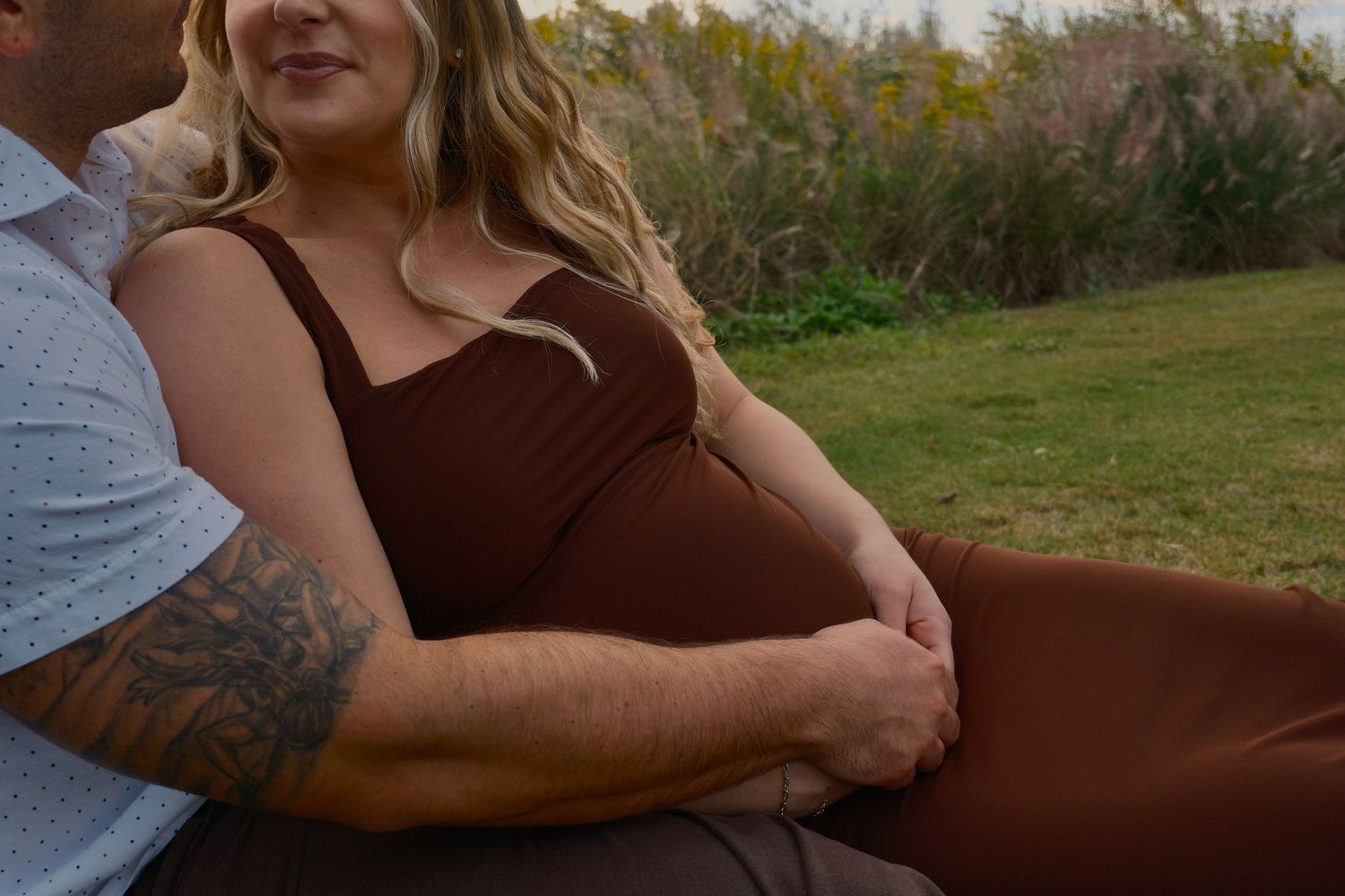 Expectant couple relaxes on the grass, the man's tattooed arm resting around the woman's baby bump.
