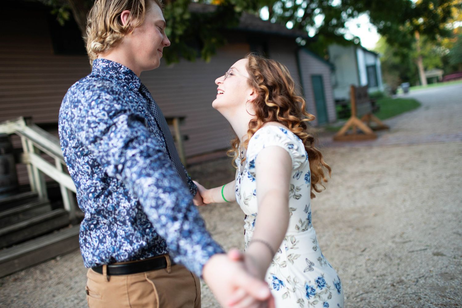 A playful couple in casual attire laughs together on a dirt path.