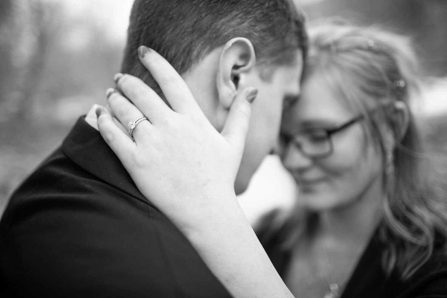 A tender black and white engagement photo showing hands with ring.