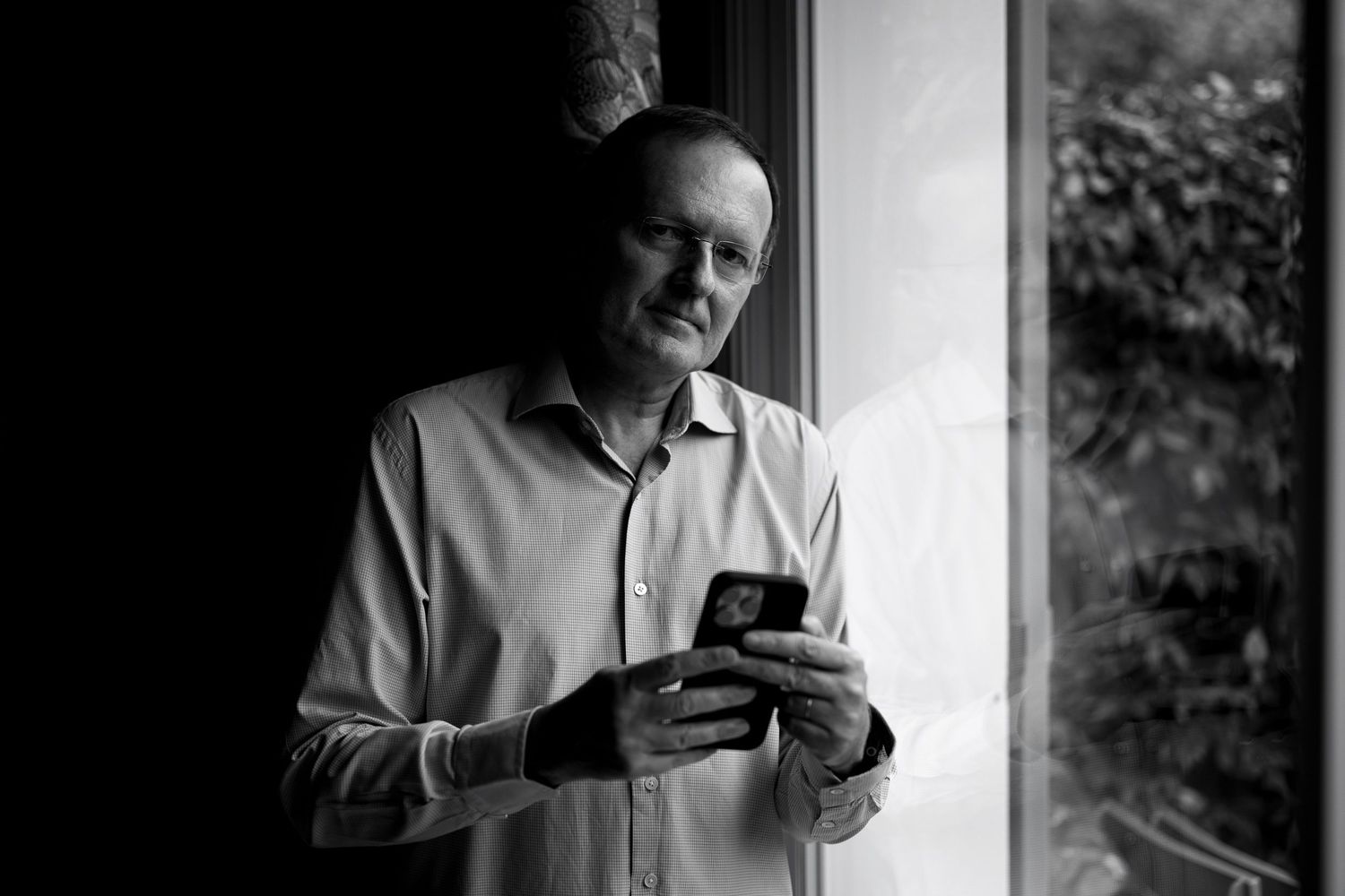 Black and white portrait of photographer Philippe Triconnet standing beside a window.
