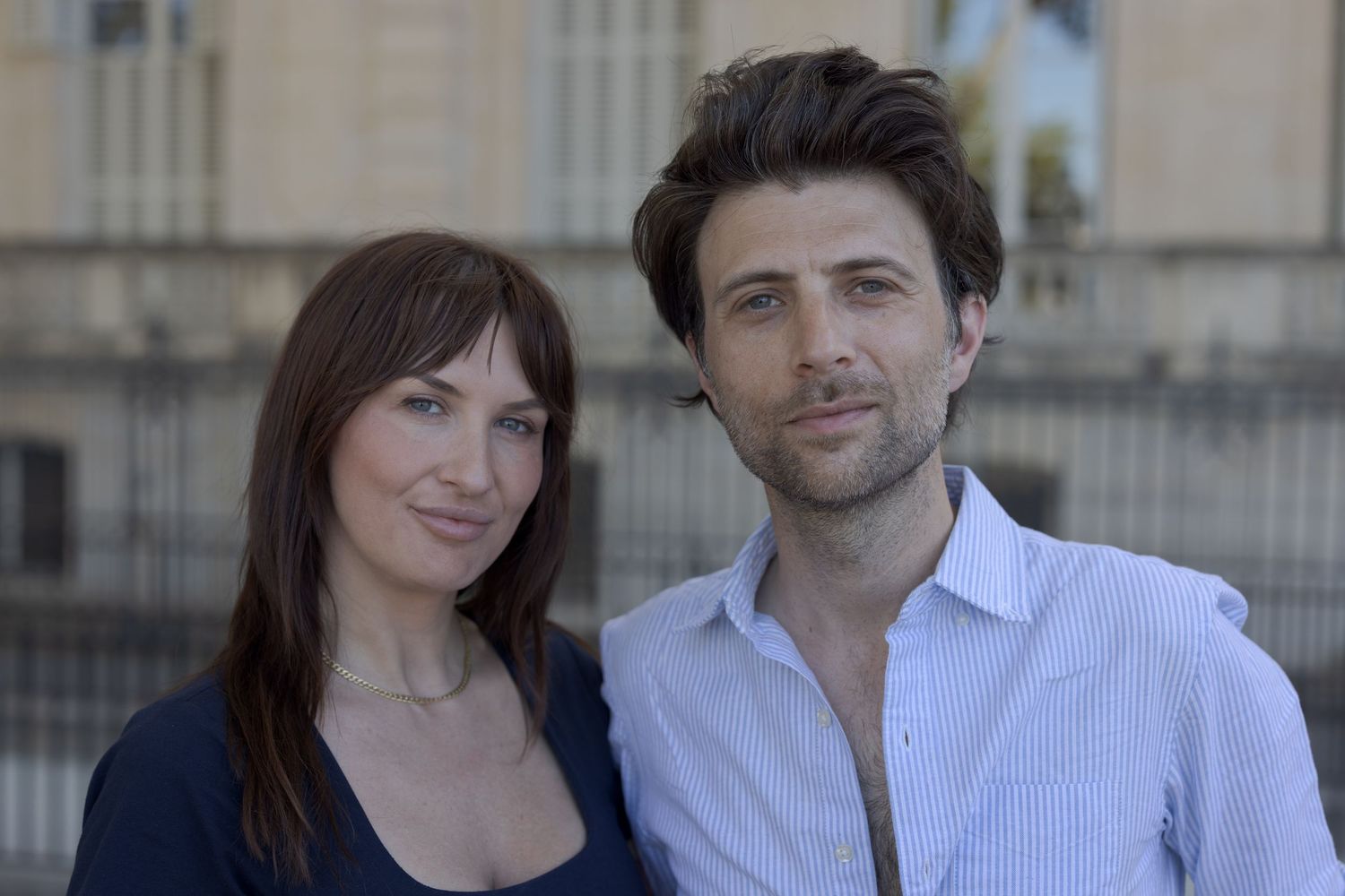 A couple standing together and looking at the camera on Quai d’Orsay in Paris.