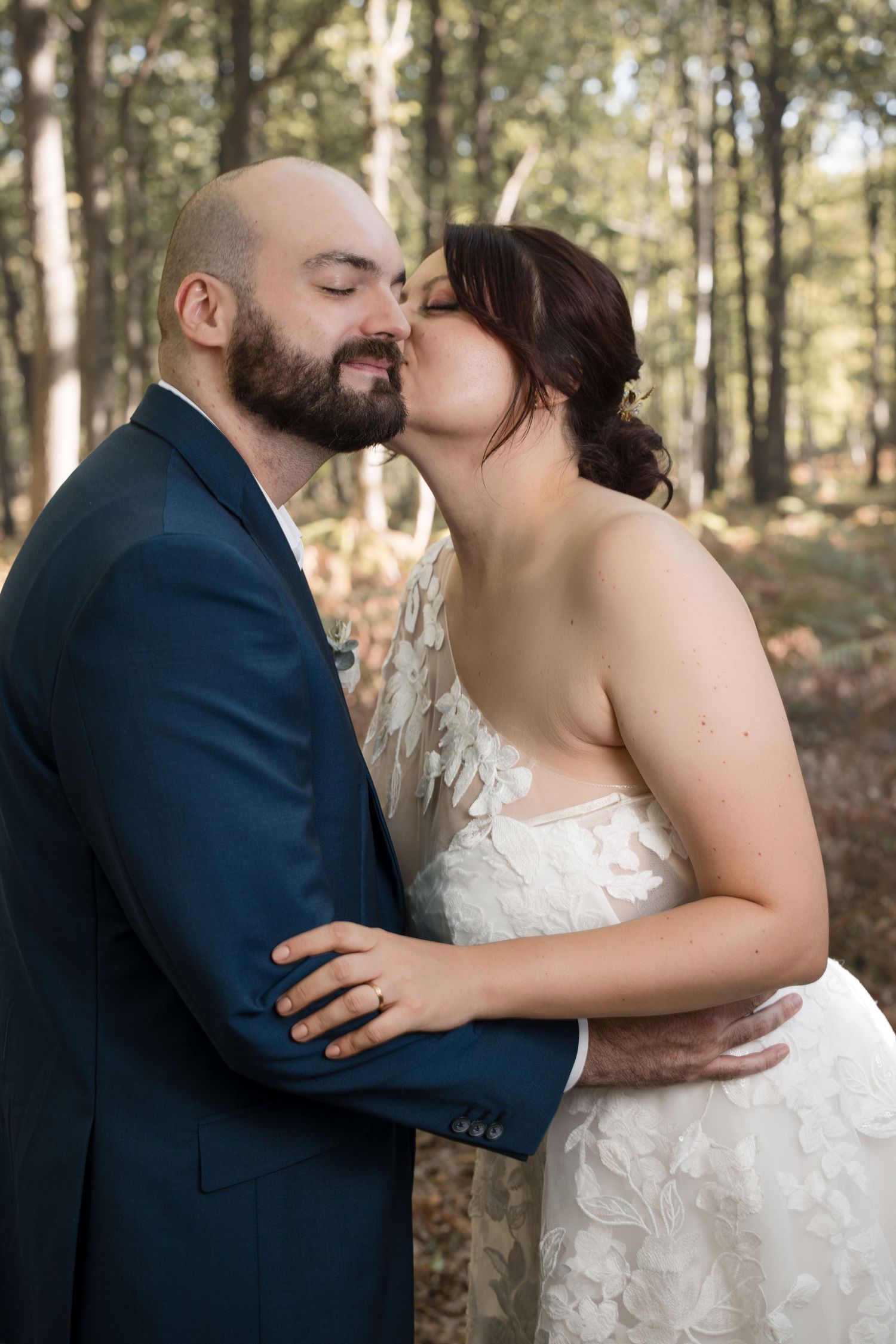 Bride kissing the groom’s cheek in the woods at La Roche Couloir in the Chevreuse Valley.