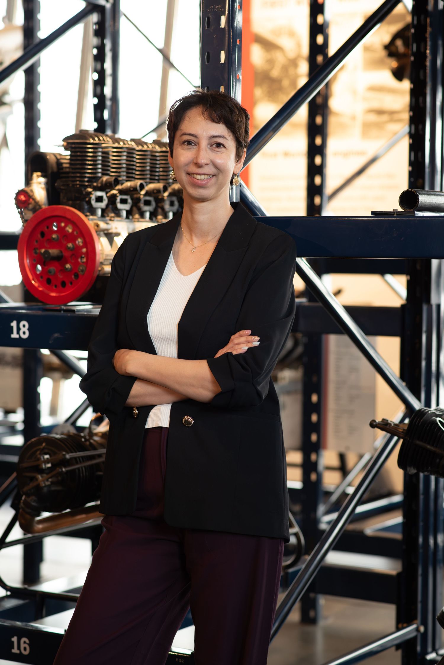 Professional woman in black blazer stands confidently with arms crossed in an industrial warehouse setting.