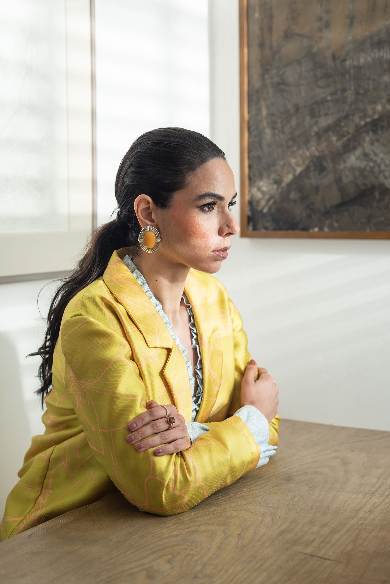 Person in bright yellow blazer rests thoughtfully on wooden table in minimalist interior setting.