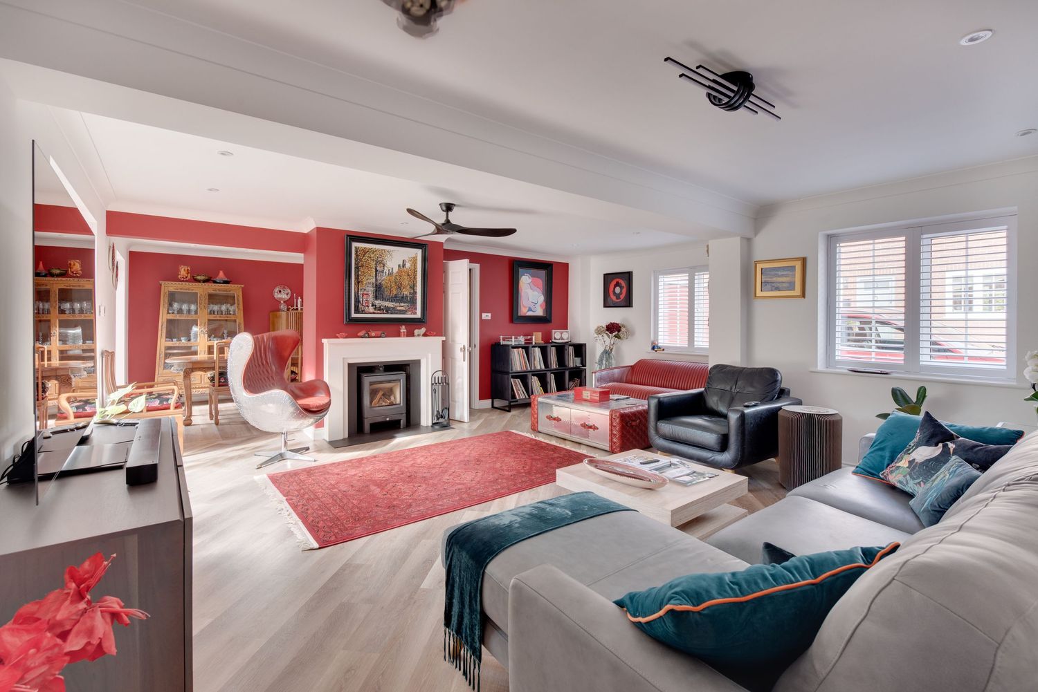 Spacious living room with red accent wall, fireplace, ceiling fan, teal cushions, and light wood flooring.
