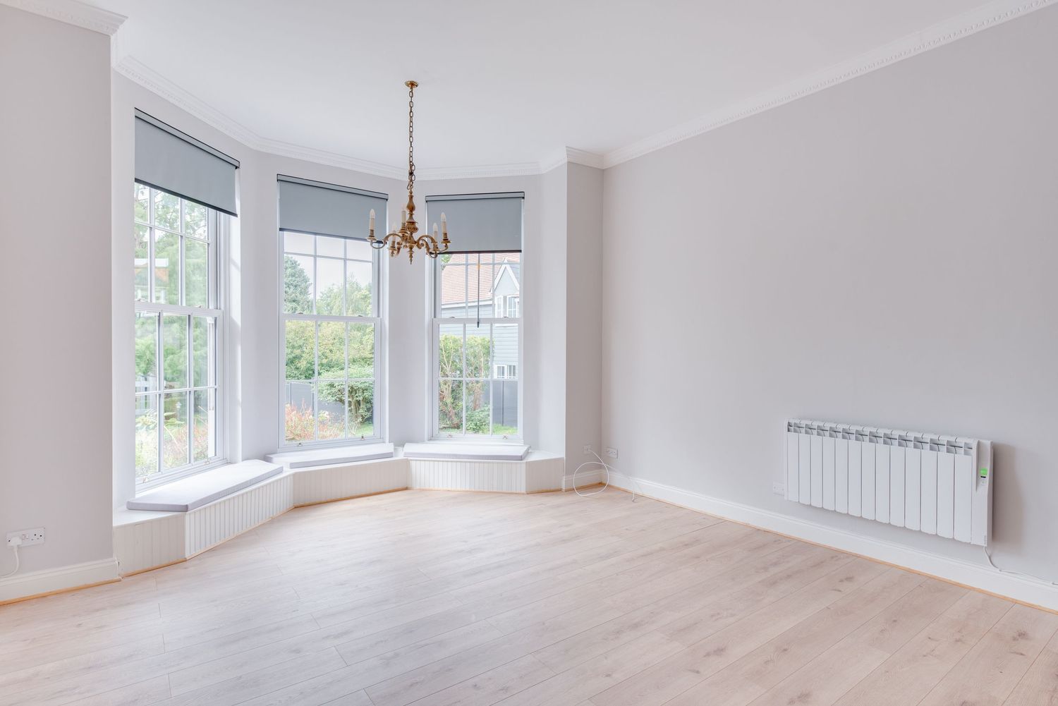 Bright empty room with bay windows, hardwood floors, chandelier, and white radiator in a modern home.