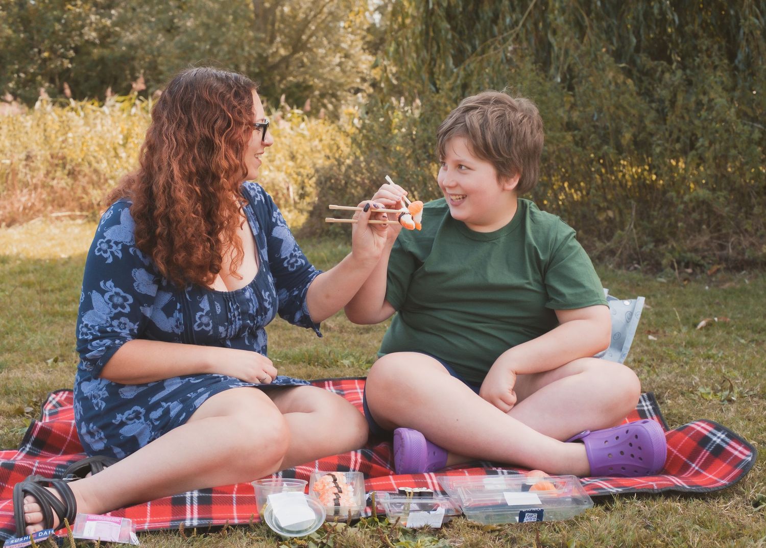 Two children enjoying a picnic on a plaid blanket outdoors, sharing food and smiling together.