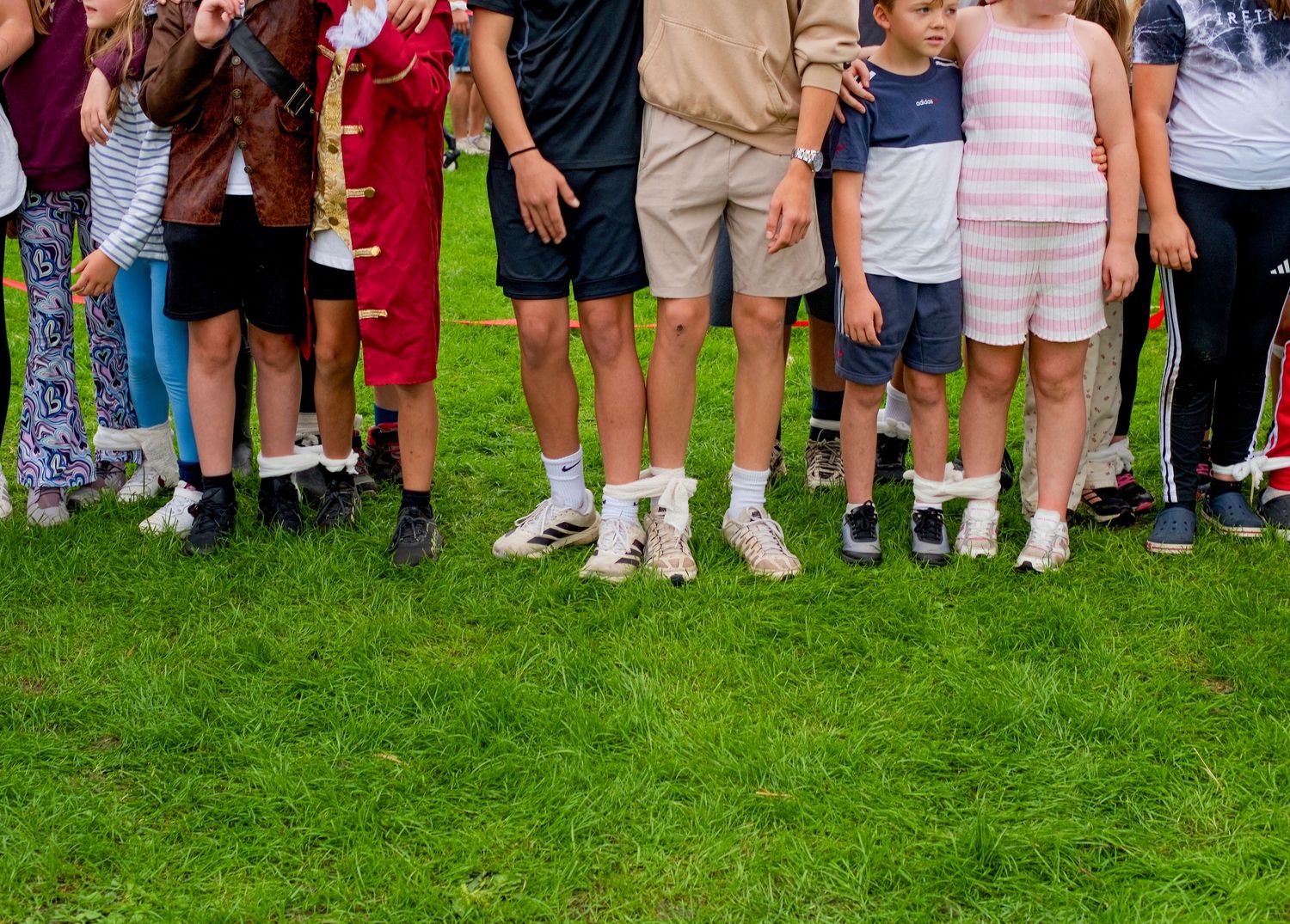 Group of children and teens standing in a row on green grass, showing colorful outfits and sneakers at an outdoor event.