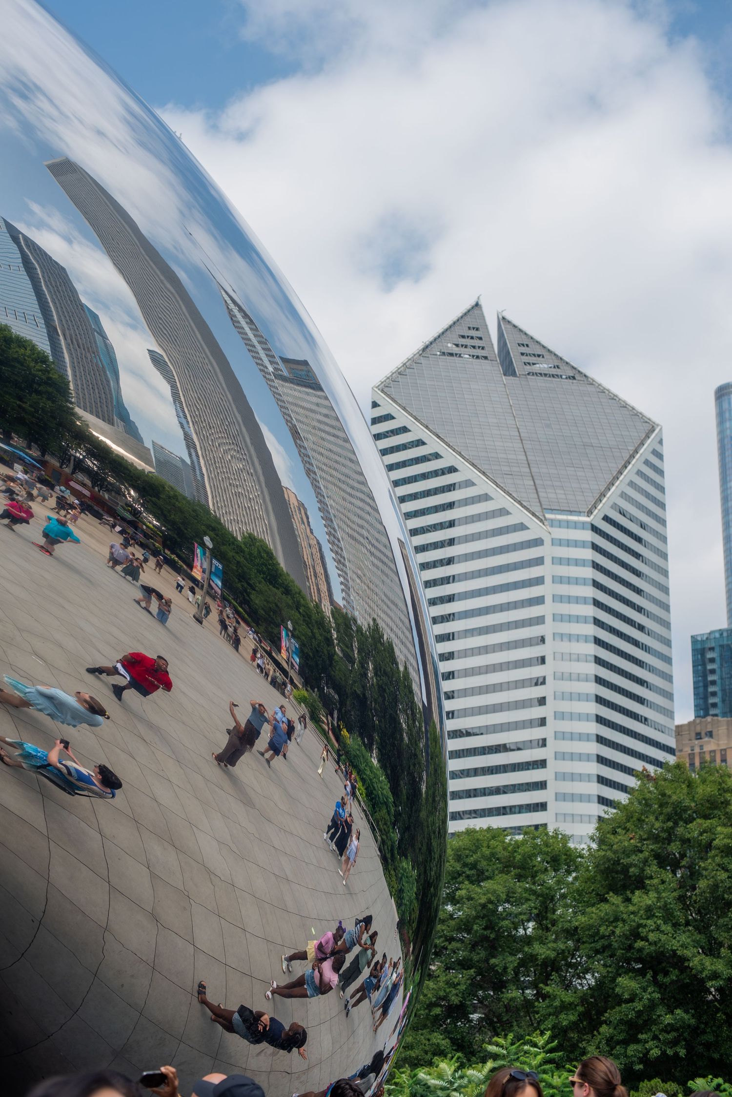 Cloud Gate sculpture in Chicago's Millennium Park reflects crowds and skyline under partly cloudy skies.