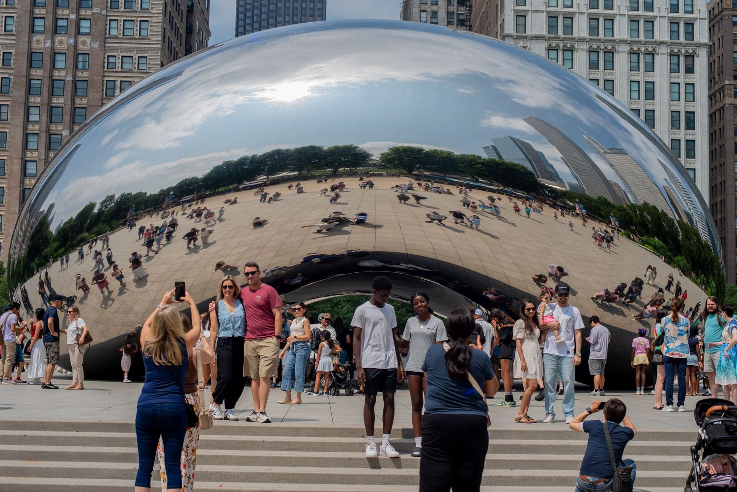 Tourists gather around Cloud Gate sculpture in Millennium Park, Chicago, reflecting the skyline and crowd.