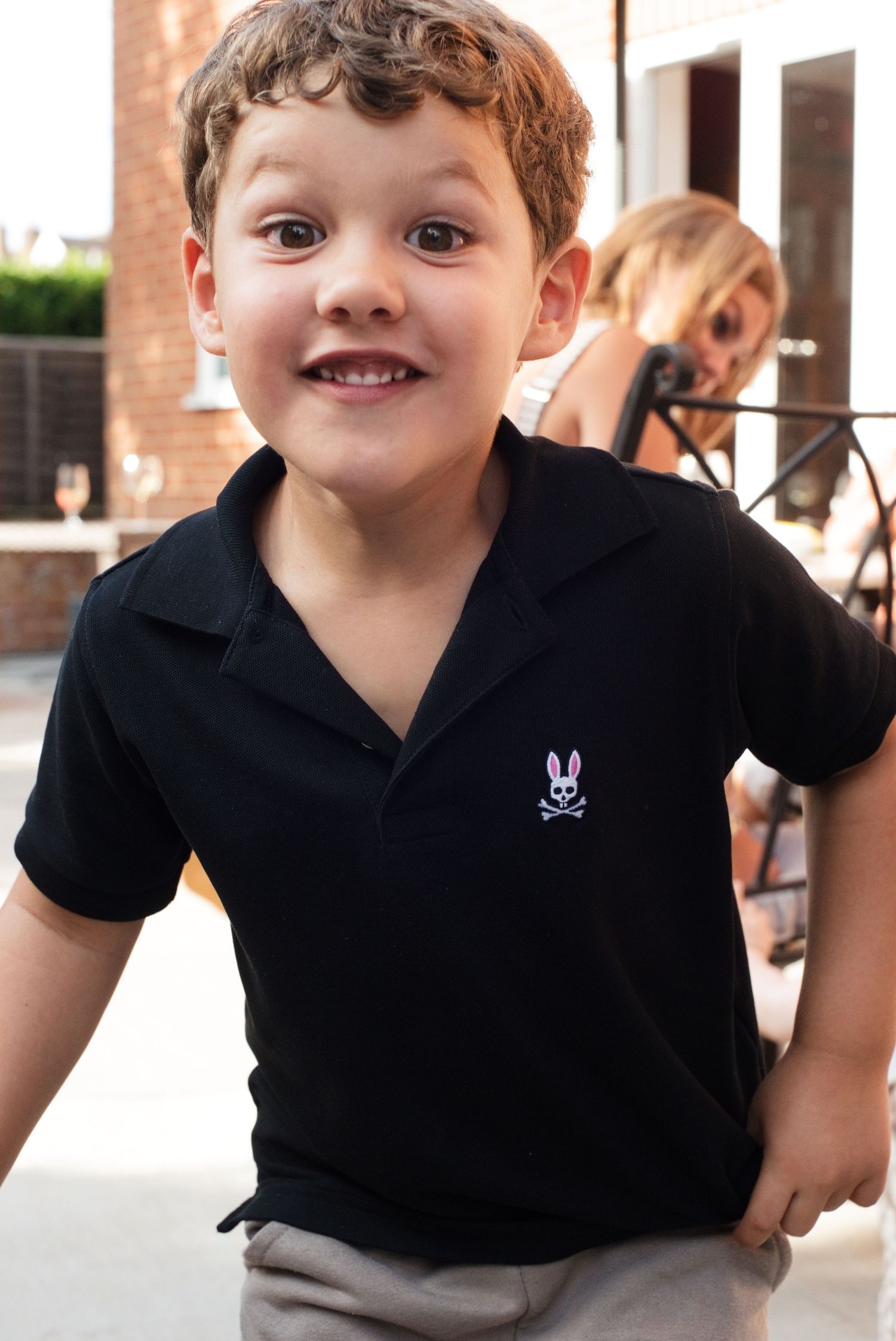 Smiling young boy wearing a black Psycho Bunny polo shirt outdoors at a casual event.