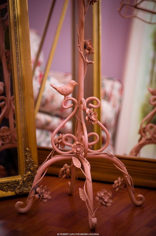 Pink ornate wrought iron candle holder with bird and floral details reflected in a gold-framed mirror.
