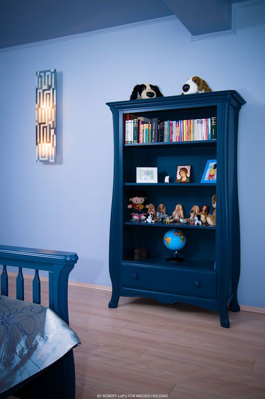 Blue bookcase with toys, books, and a globe in a child's room with light wood floors and blue walls.