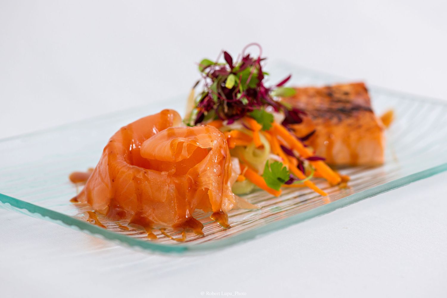 Elegant plated salmon dish with glazed cured salmon, seared fillet, julienned carrots, and microgreens on a glass plate.