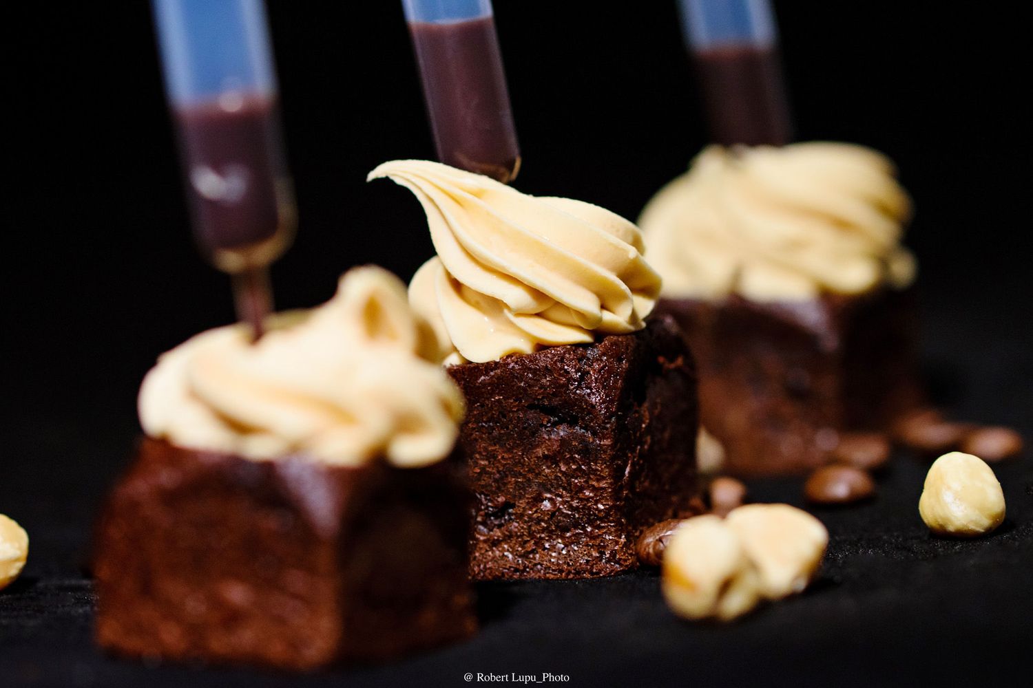 Chocolate brownies topped with creamy peanut butter frosting, garnished with hazelnuts on a dark slate surface.