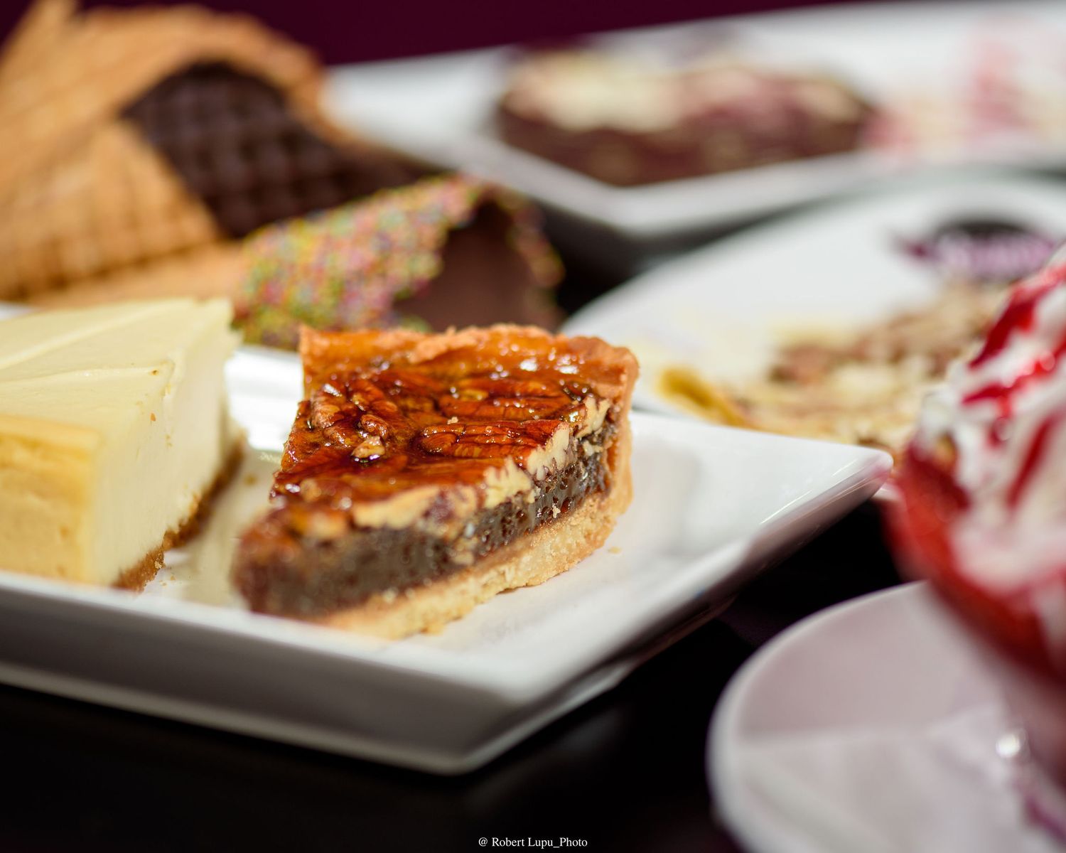 Assorted desserts on a white plate featuring pecan pie slice, cheesecake, and chocolate treats at a dessert buffet.