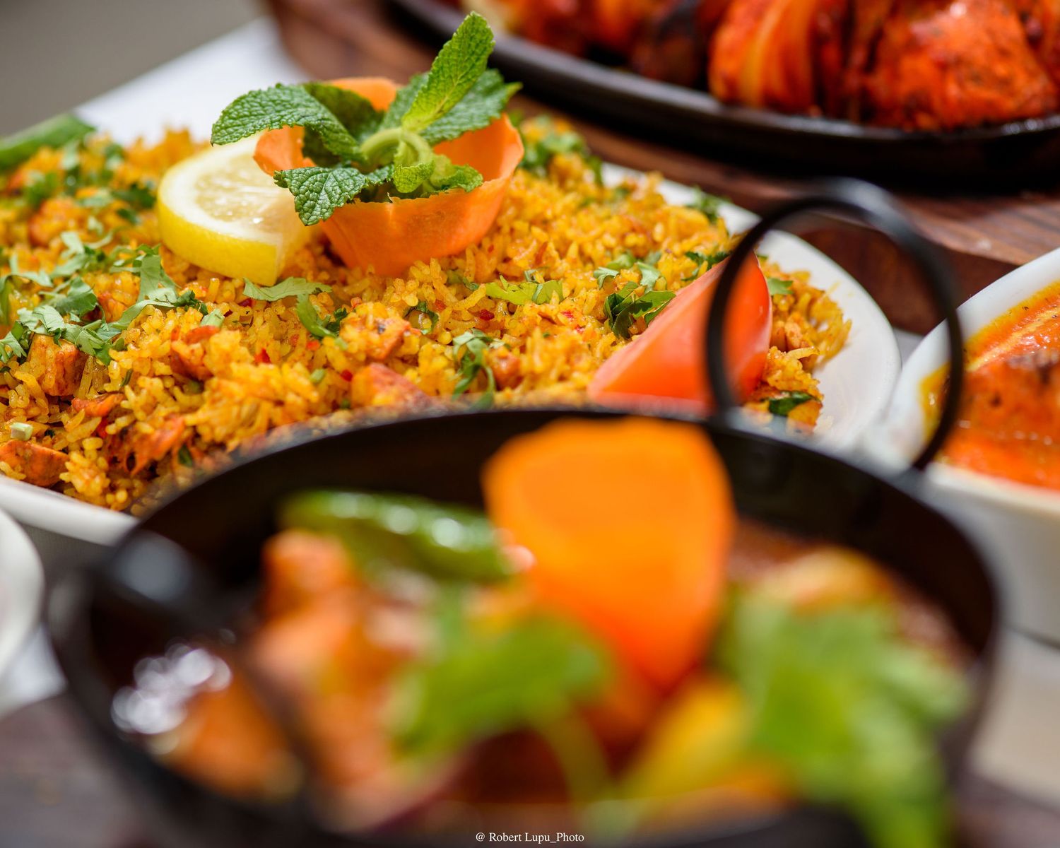 Vibrant saffron biryani rice garnished with mint and lemon alongside colorful Indian dishes.
