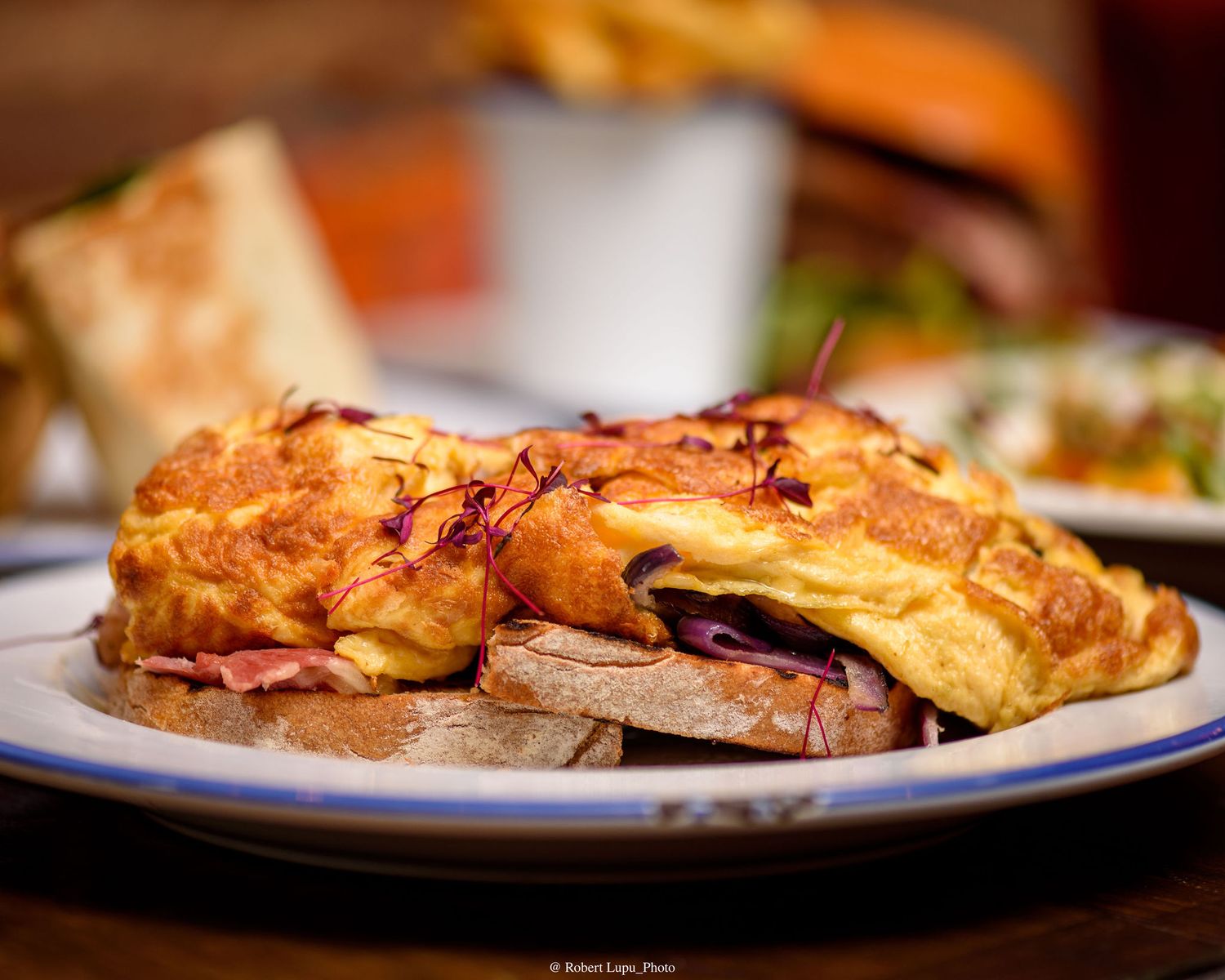 Golden omelette with ham on toasted bread served on a white plate at a restaurant.