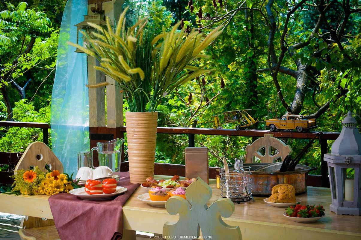 Outdoor terrace dining table with tropical decor, fresh pastries, and lush green forest backdrop.