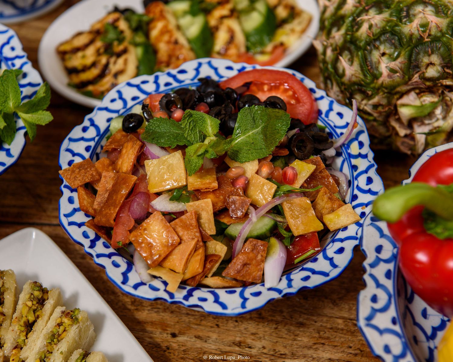 Colorful Middle Eastern fattoush salad with crispy pita, tomatoes, cucumbers, olives, and fresh mint on a decorative plate.