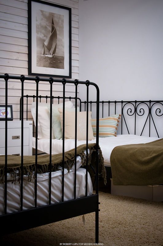 Vintage-style hotel room with black iron beds, striped pillows, and nautical wall art.