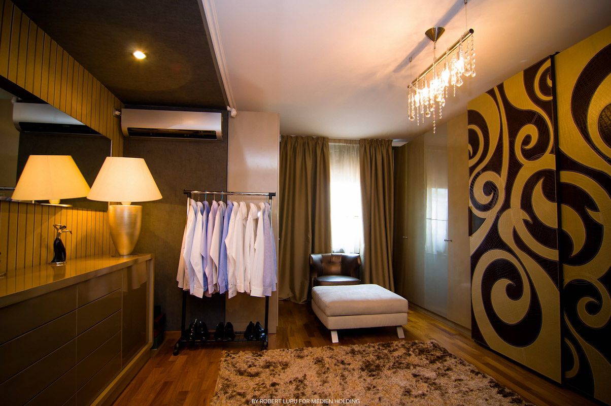Elegant hotel dressing room with clothes rack, chandelier, decorative wall panel, and chaise lounge on hardwood floors.