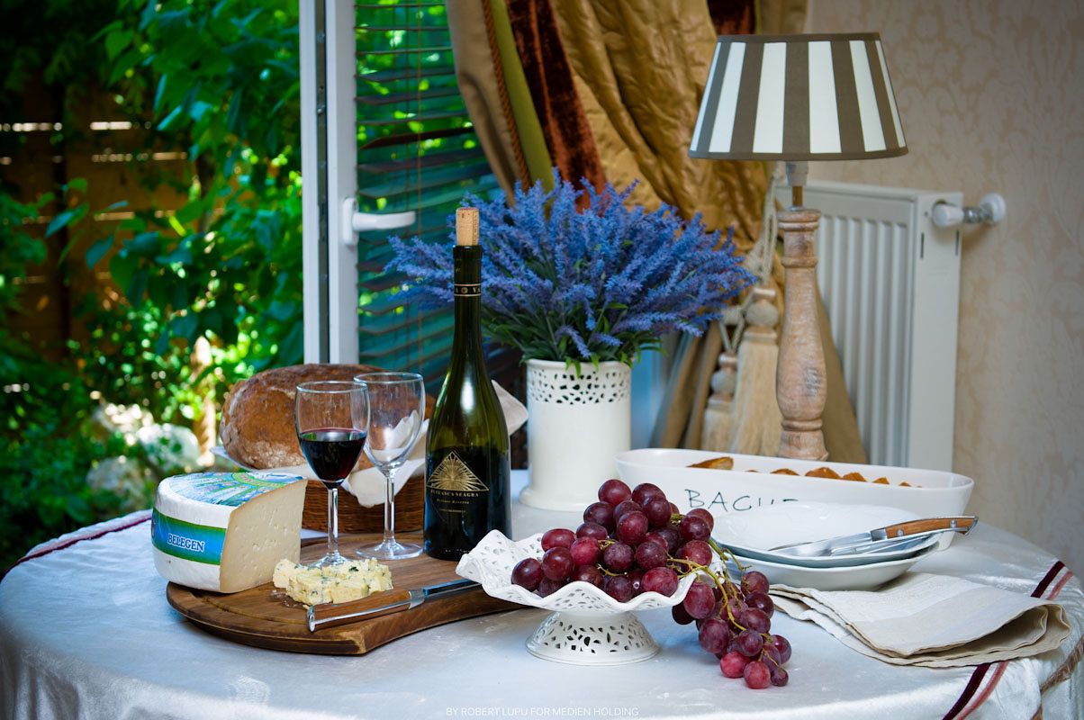 Elegant French table setting with red wine, cheese board, grapes, lavender bouquet, and lamp on white tablecloth.
