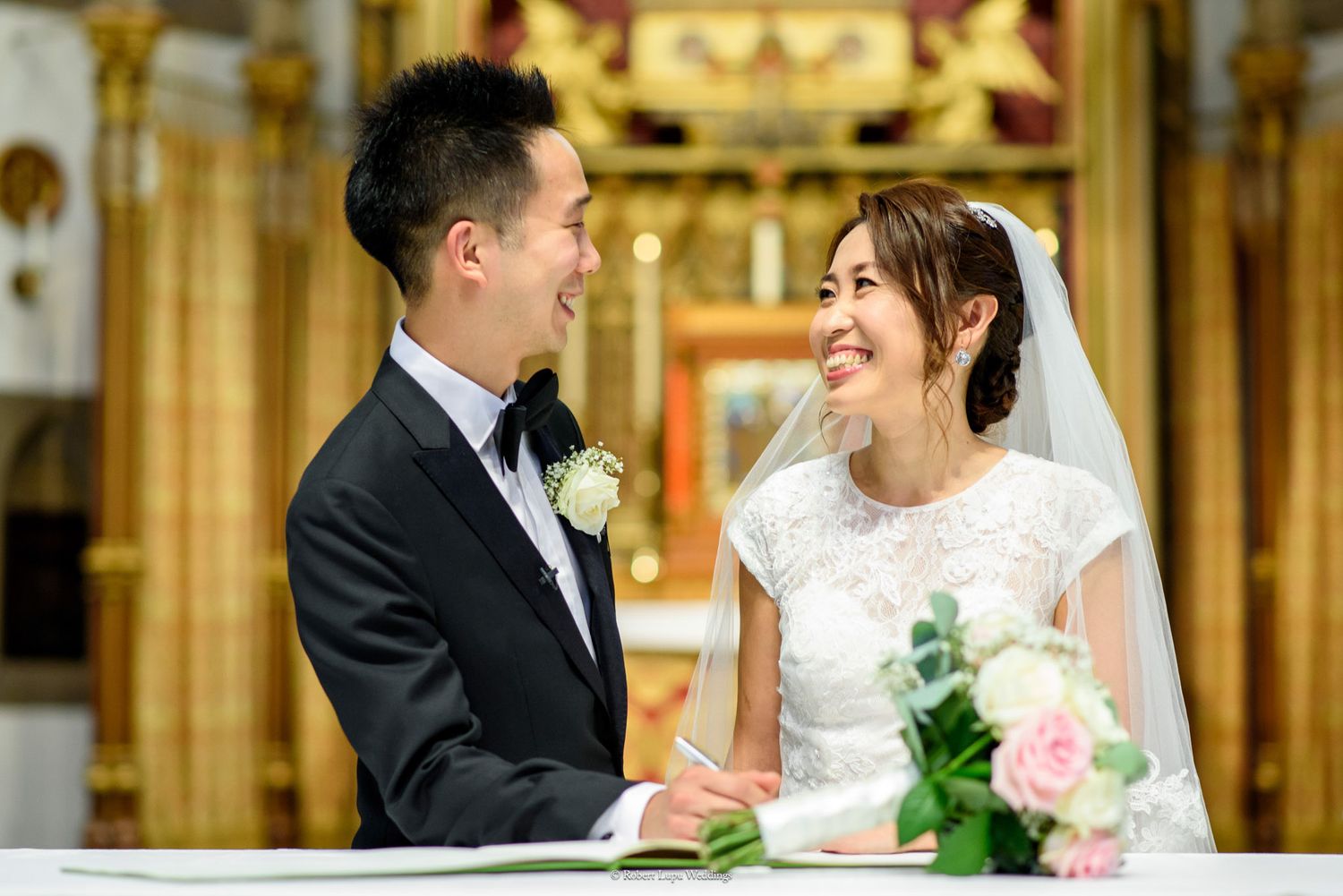 Smiling Asian bride and groom exchanging vows at elegant church wedding ceremony altar.