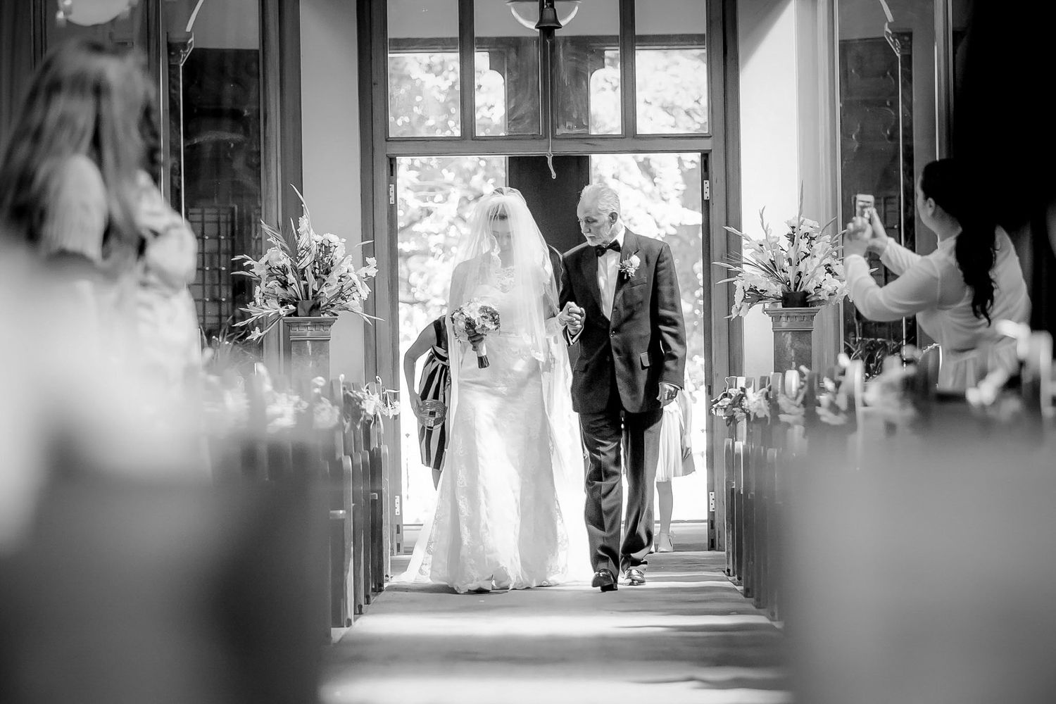 Black and white photo of a bride walking down the church aisle with her father on her wedding day.