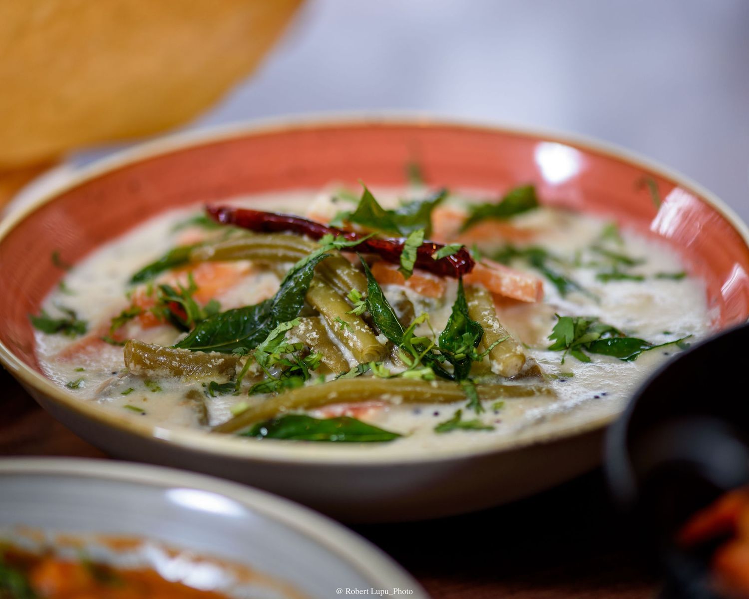 Creamy Indian curry with vegetables, fresh herbs, and red chili in a pink bowl.