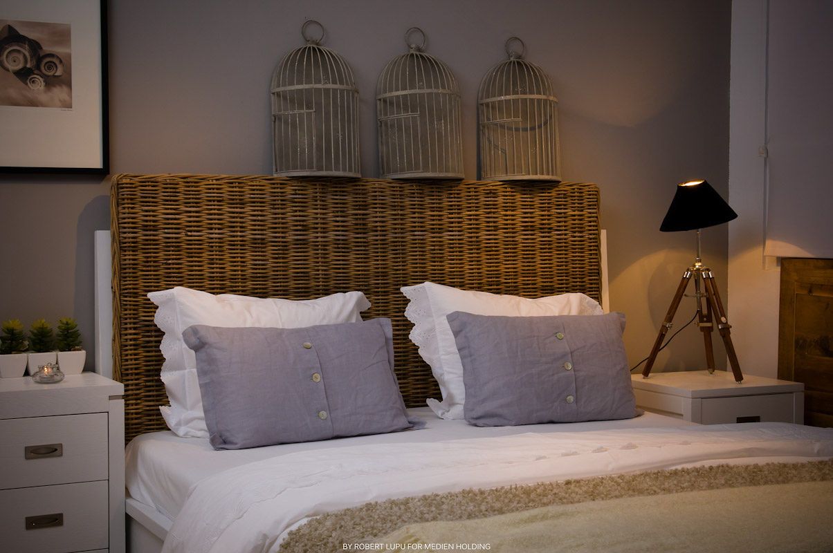Cozy bedroom with wicker headboard, white bedding, gray pillows, and decorative bird cages mounted on the wall.