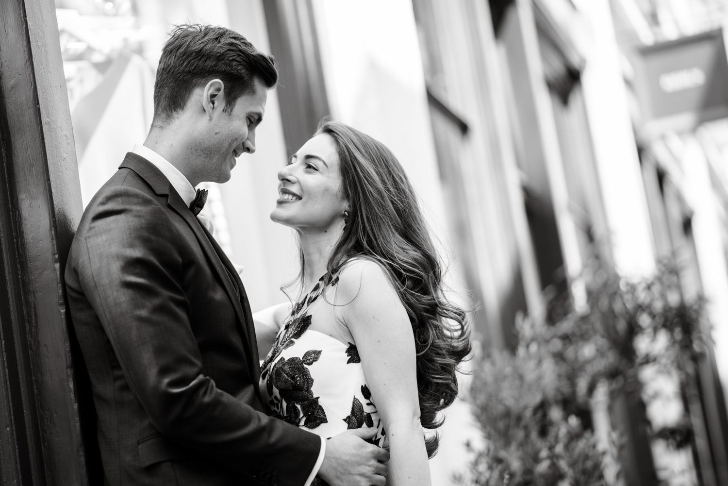 Black and white photo of a smiling couple in formal attire sharing a romantic moment outdoors.
