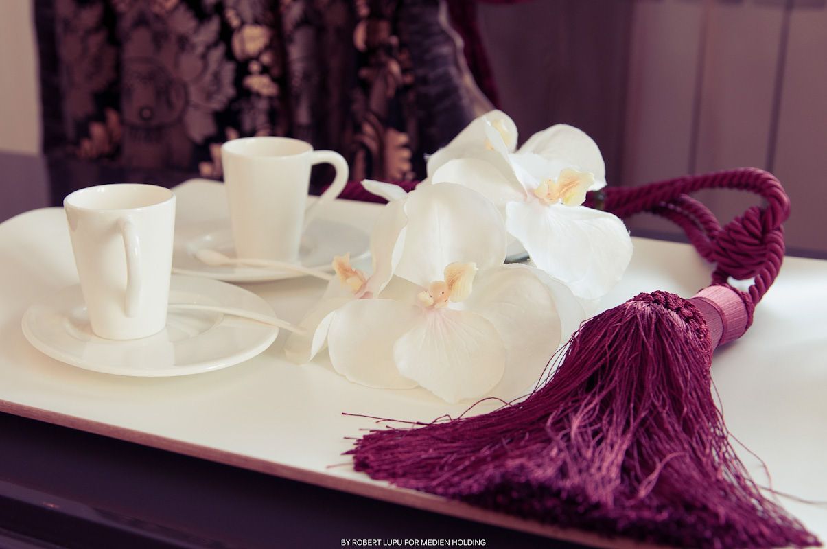 Elegant white coffee cups with orchid flowers and burgundy tassel on a white tray.