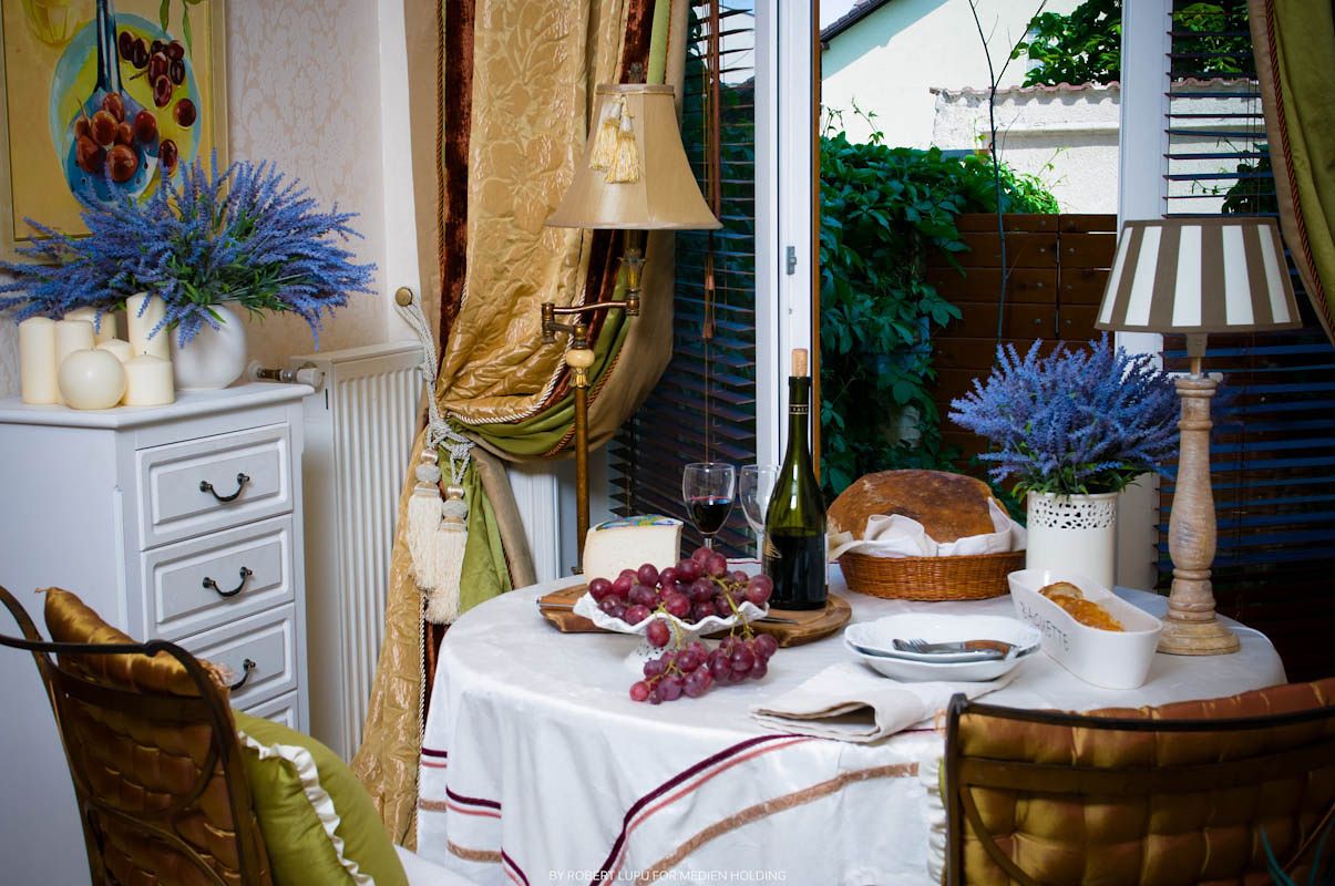 Elegant dining table with white tablecloth, wine, grapes, bread, and lavender flowers in a cozy French-style room.