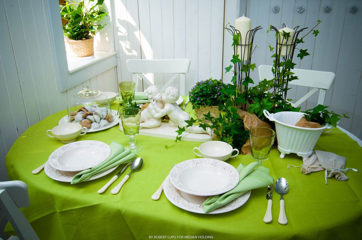 Elegant green table setting with white plates, silverware, and fresh plants on a lime green tablecloth.