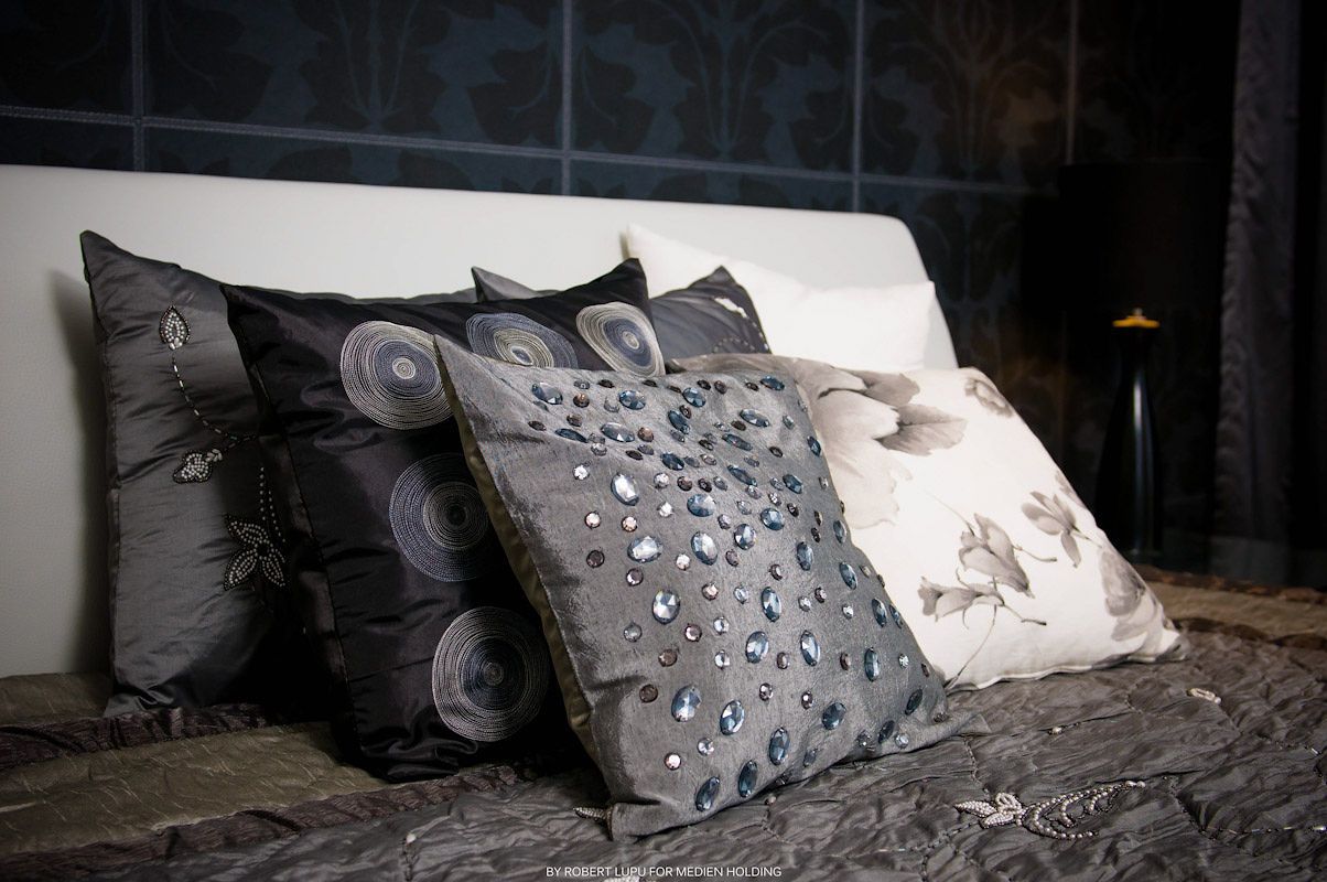 Decorative throw pillows in gray and silver tones with embellishments displayed on a bed with dark bedding.