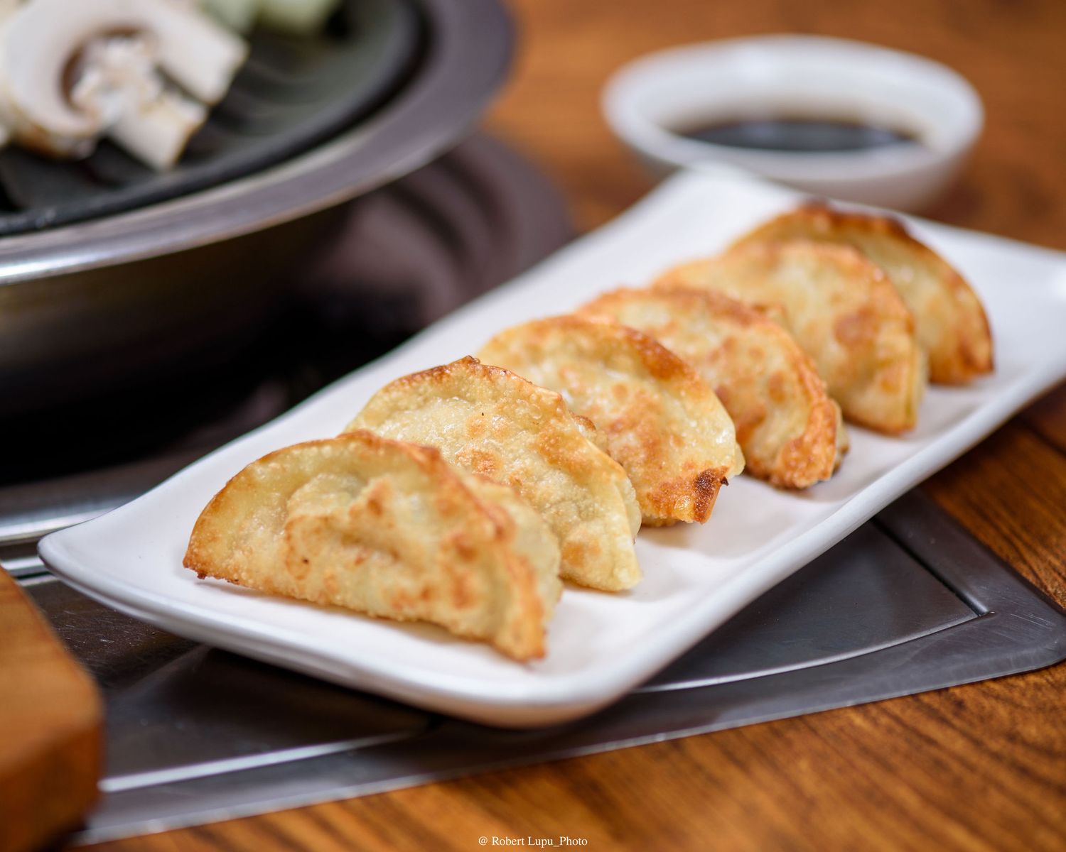 Golden pan-fried potsticker dumplings served on a white rectangular plate with dipping sauce in background.
