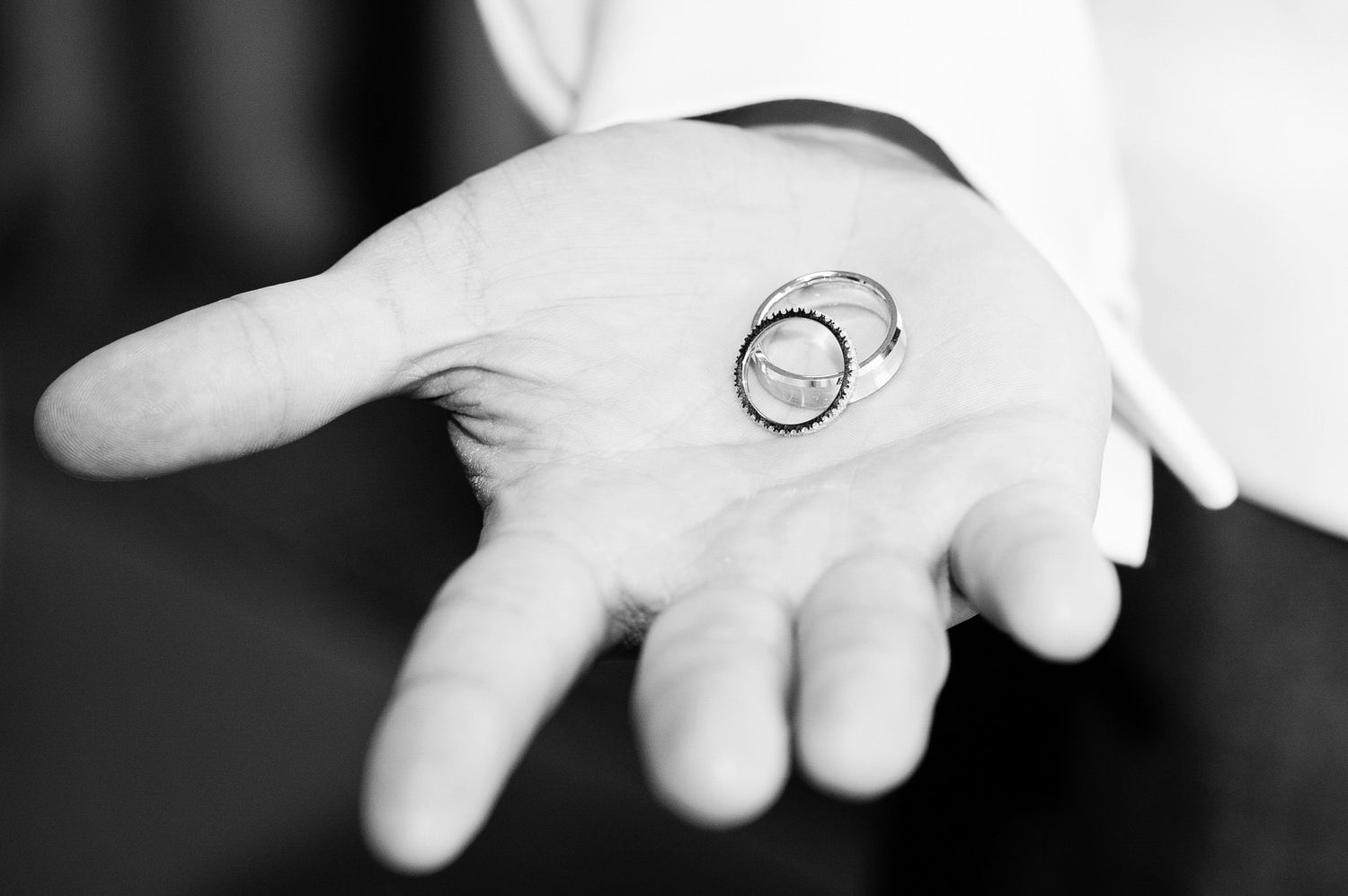 Black and white photo of a groom holding two wedding rings in his open palm.