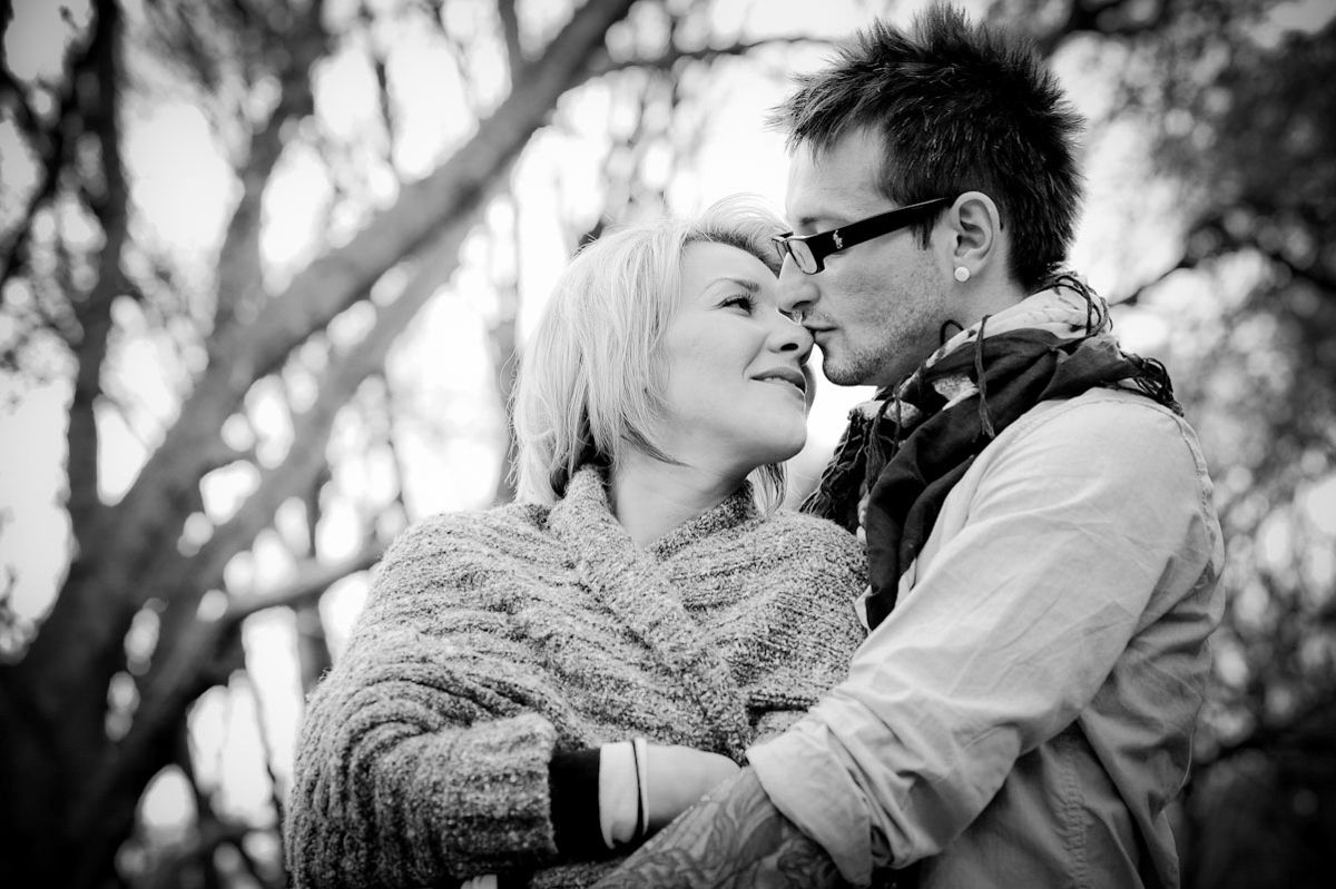 Black and white photo of a romantic couple embracing outdoors, woman in knit wrap smiling as man leans in close.