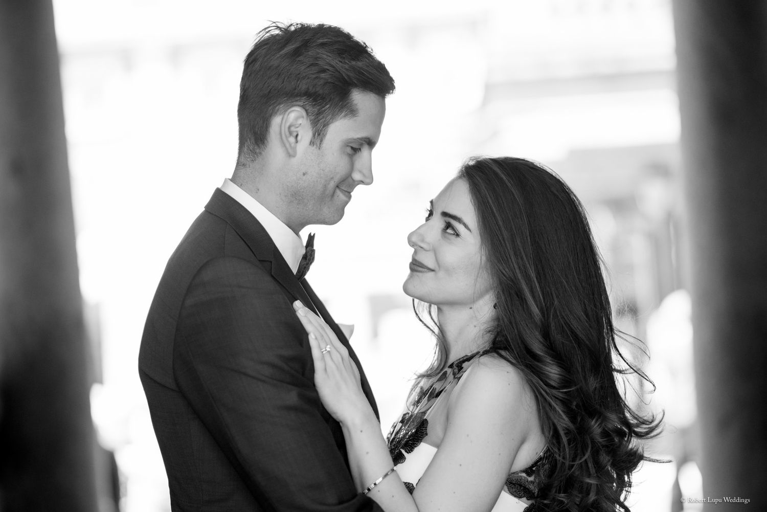 Black and white photo of an elegant couple in formal attire sharing a romantic moment, woman gazing up at man.