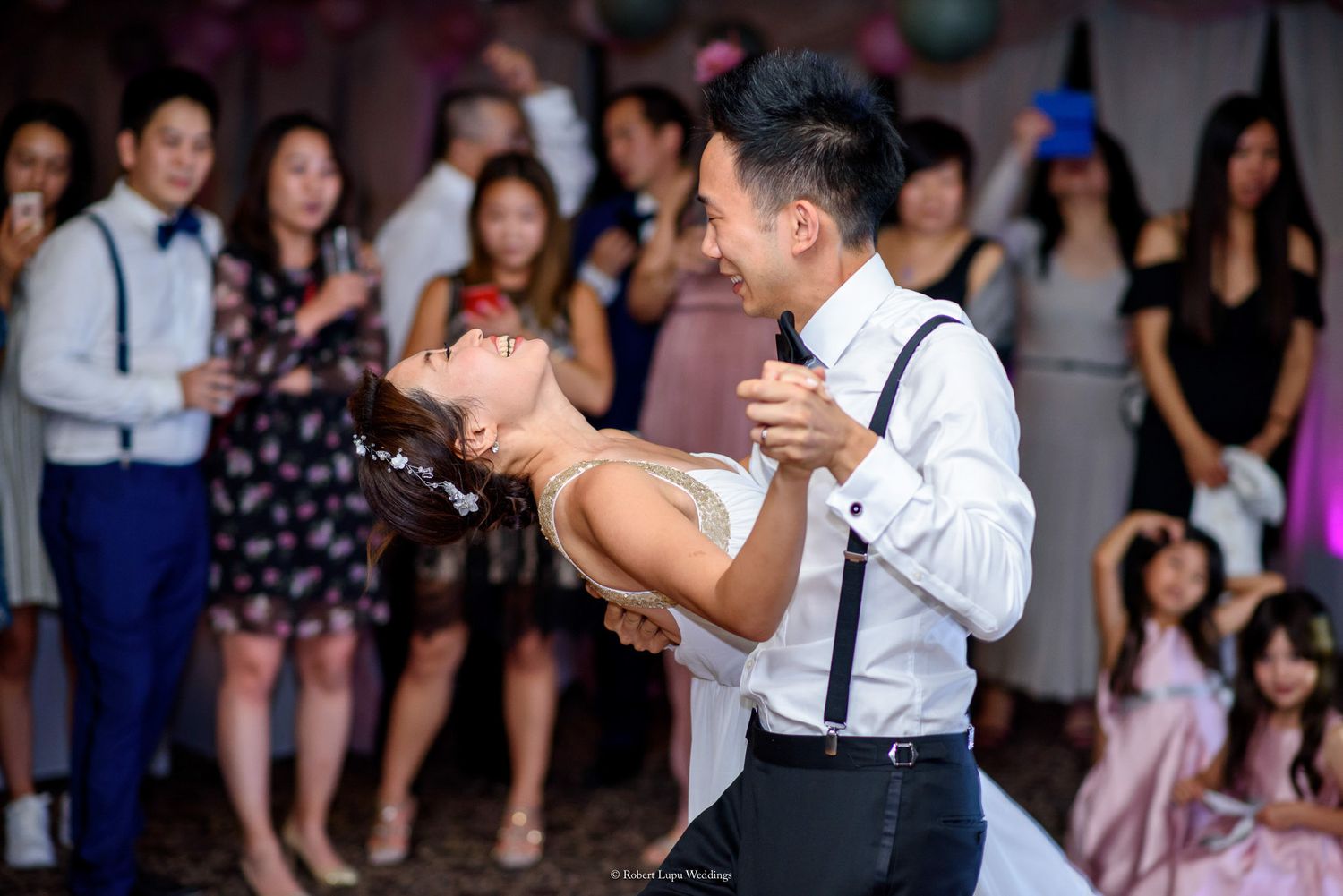 Couple shares romantic first dance at wedding reception, with guests watching in background.