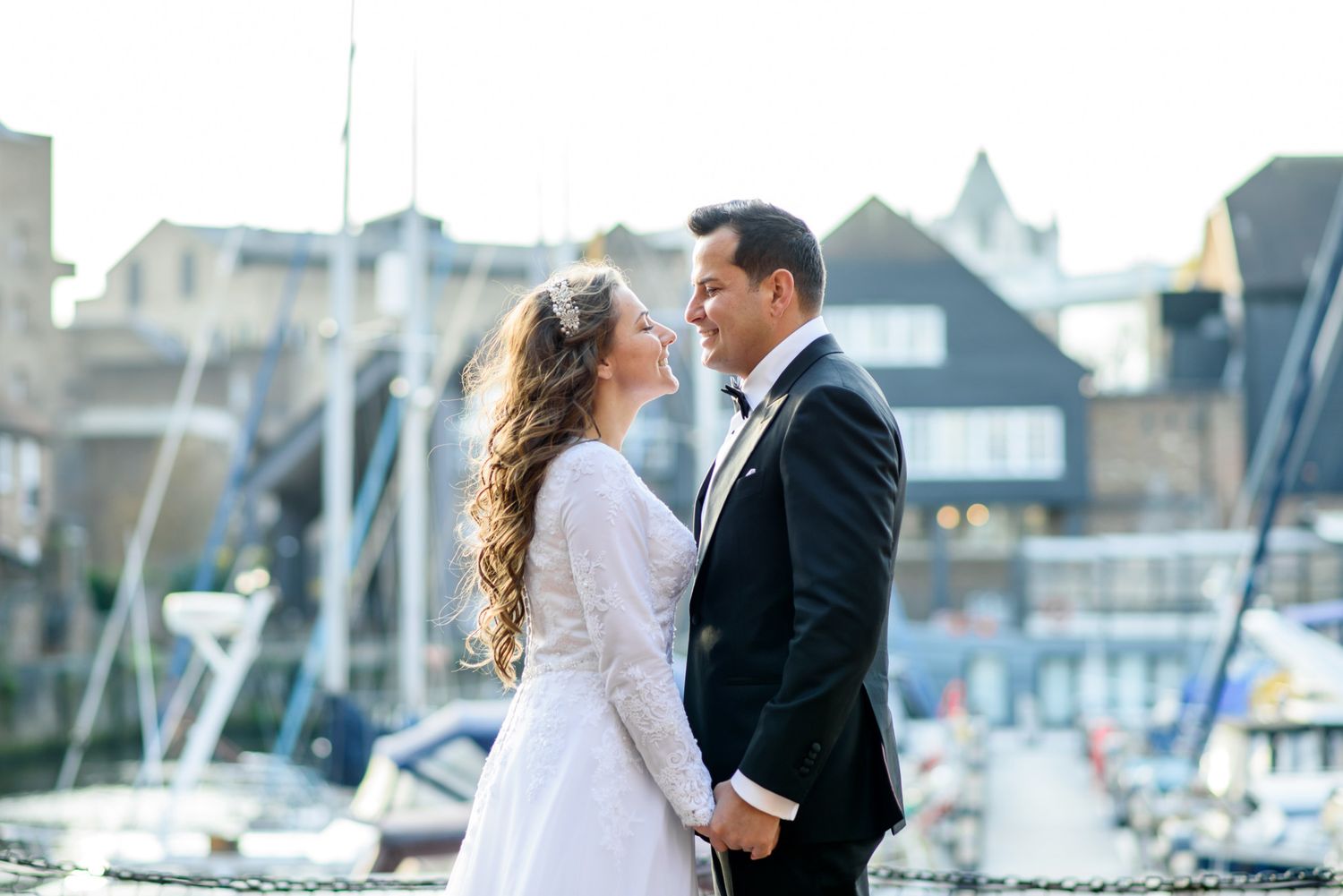 Elegant wedding couple holding hands at a marina, bride in white gown and groom in black tuxedo.