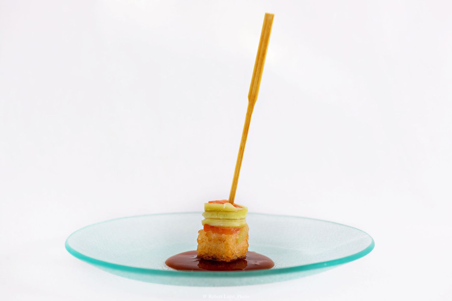 Elegant gourmet appetizer with crispy base, apple slice, and caramel sauce on a glass plate, garnished with a breadstick.