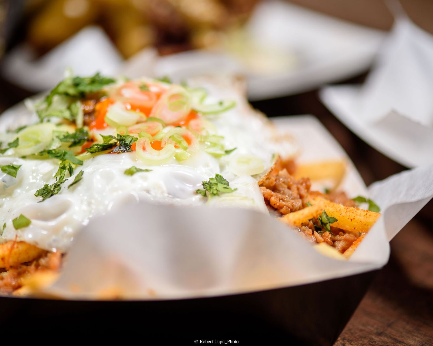 Loaded nachos topped with sour cream, fresh salsa, green onions, and cilantro served in a paper-lined basket.
