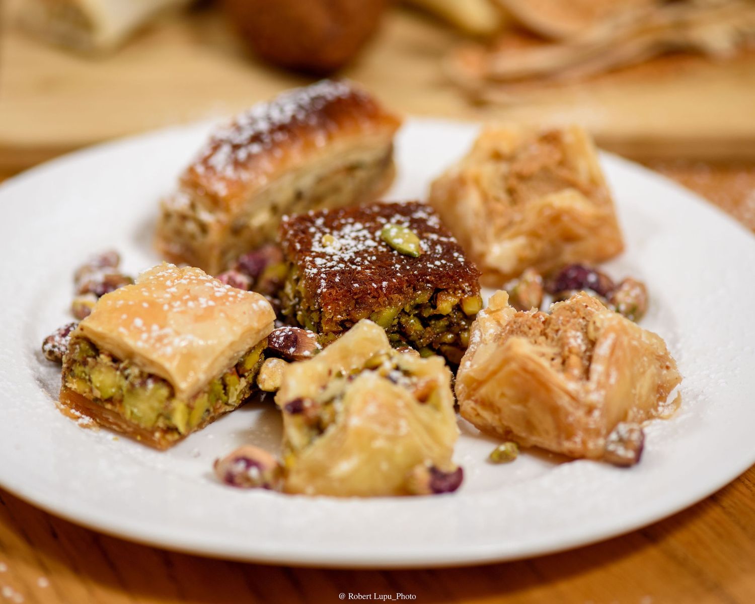 Assorted baklava pieces with pistachios and nuts, dusted with powdered sugar, served on a white plate.