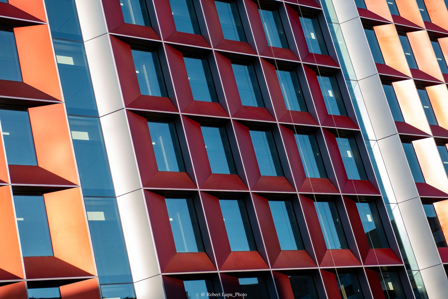 Modern building facade with geometric red, orange, and blue rectangular windows reflecting sunlight.