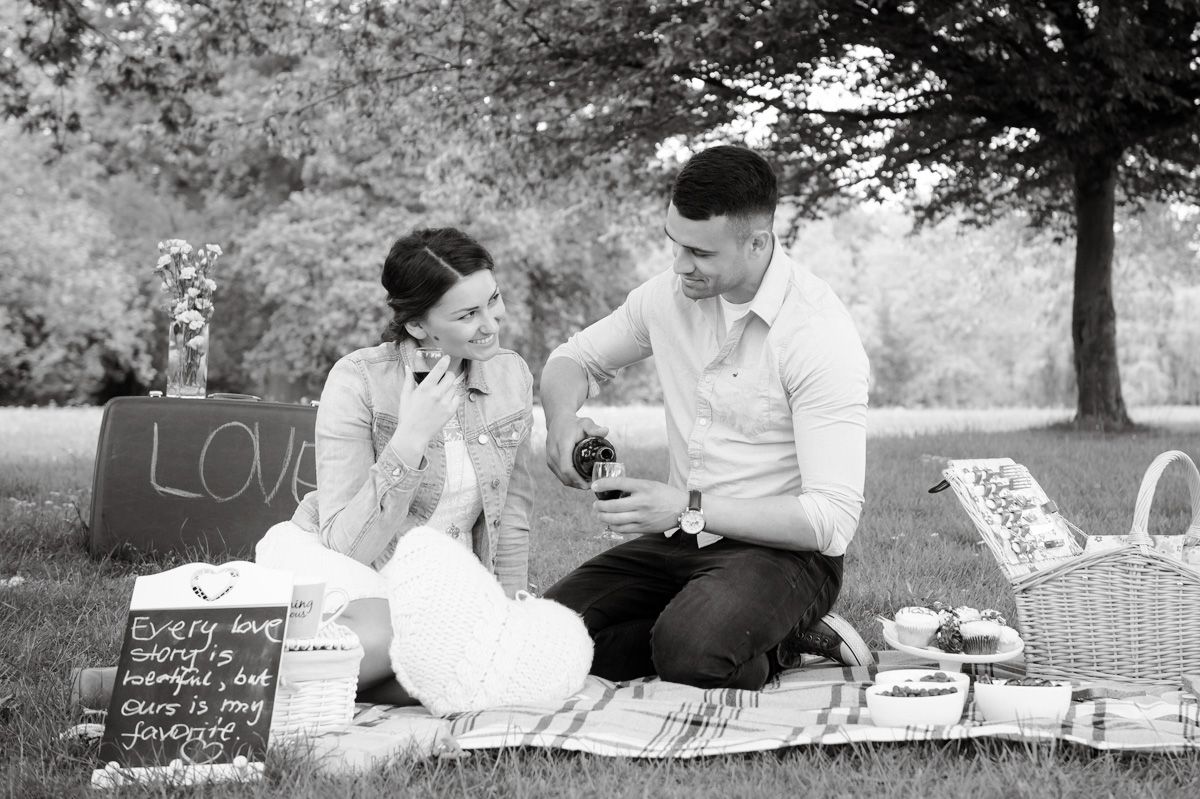 Couple enjoying a romantic black and white picnic in the park with a love sign and basket.